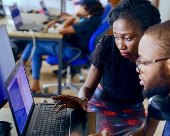 Zwei Personen arbeiten zusammen an Computern in einem modernen Büro, während sie Code auf Bildschirmen überprüfen und diskutieren.