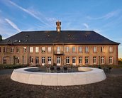 Historic building with a clock tower, surrounded by a circular seating area and a paved space.