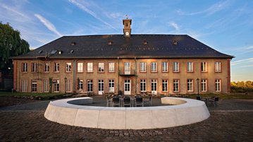 Historic building with a clock tower, surrounded by a circular seating area and a paved space.
